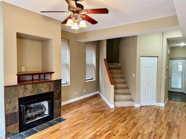 unfurnished living room with ceiling fan, light wood-type flooring, a wealth of natural light, and a tiled fireplace