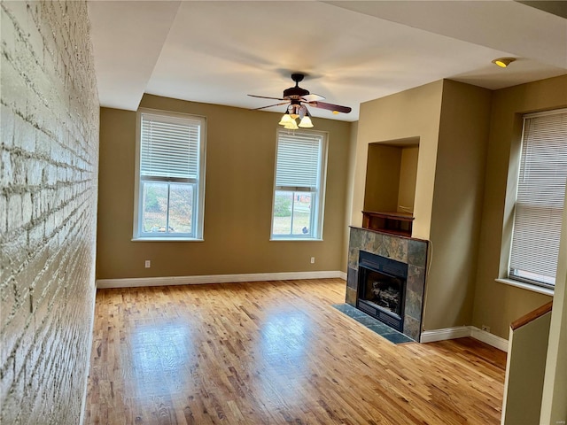 unfurnished living room with ceiling fan, light wood-type flooring, and a tiled fireplace