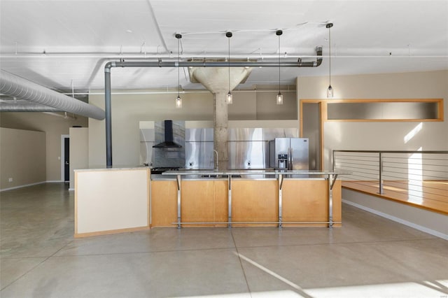 kitchen with wall chimney exhaust hood, concrete flooring, sink, decorative light fixtures, and stainless steel fridge with ice dispenser