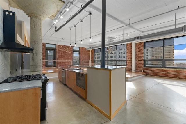 kitchen featuring brick wall, black gas stove, an island with sink, and range hood