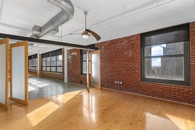 spare room featuring ceiling fan, plenty of natural light, wood-type flooring, and brick wall