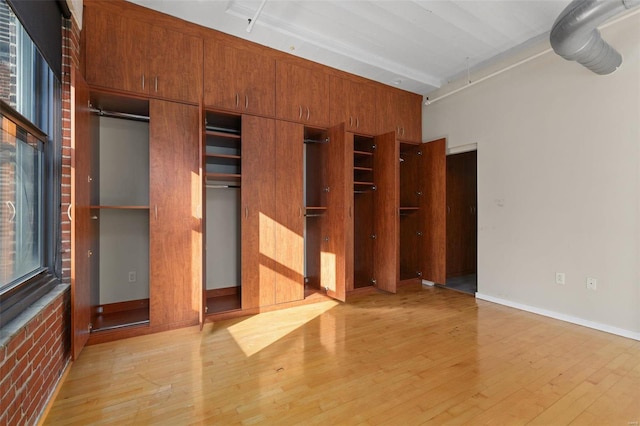 unfurnished bedroom with light hardwood / wood-style floors and brick wall