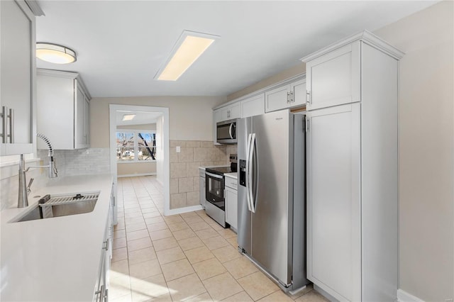 kitchen featuring stainless steel appliances, sink, light tile patterned floors, white cabinetry, and lofted ceiling