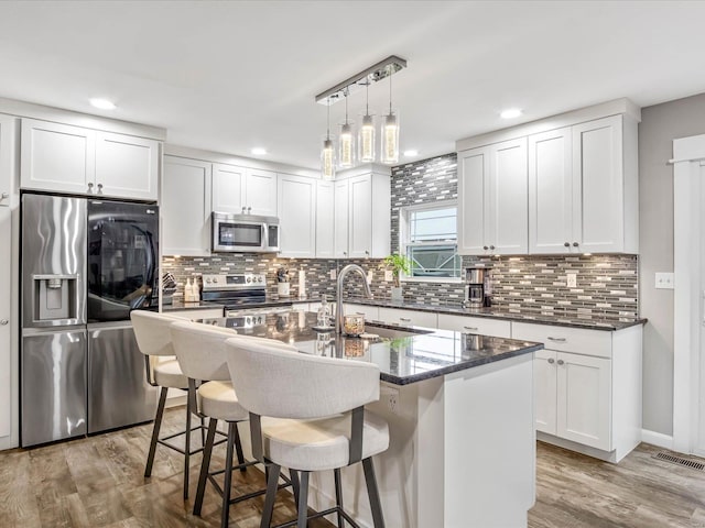 kitchen featuring appliances with stainless steel finishes, backsplash, hardwood / wood-style floors, white cabinetry, and an island with sink