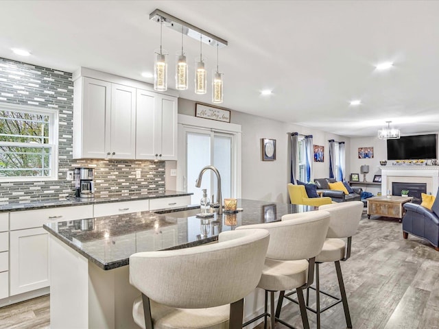 kitchen with sink, an island with sink, dark stone counters, white cabinets, and light wood-type flooring