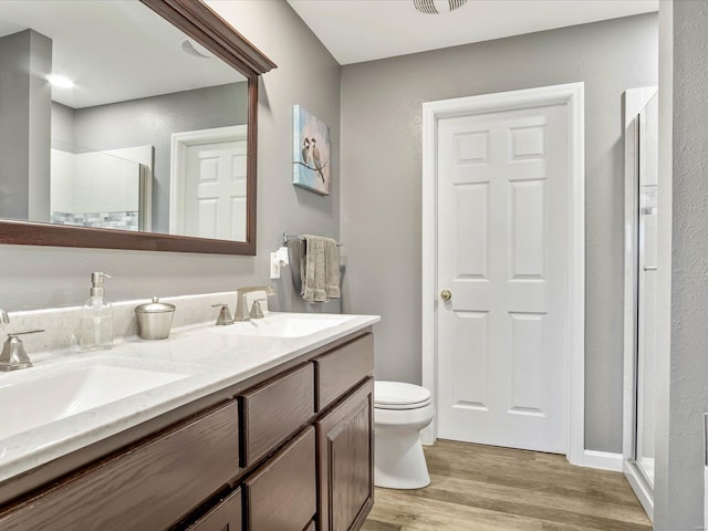 bathroom with a shower with door, vanity, wood-type flooring, and toilet