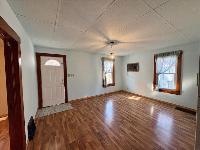 foyer entrance featuring an AC wall unit, a drop ceiling, and wood-type flooring