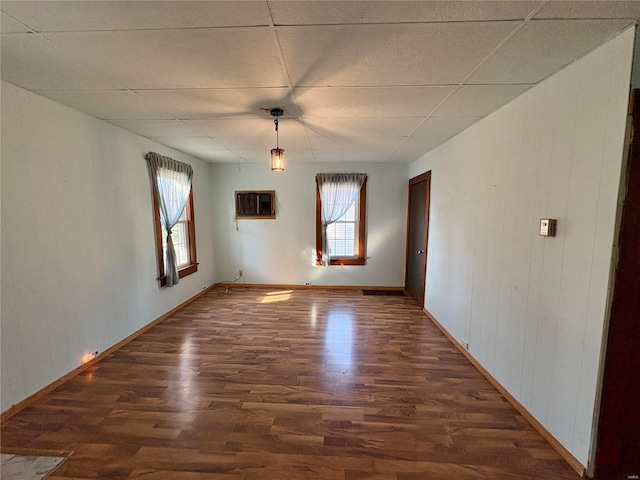 unfurnished room featuring dark hardwood / wood-style floors, a drop ceiling, and a wall unit AC