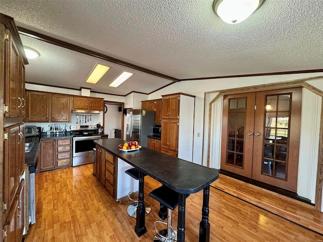 kitchen featuring stainless steel appliances, vaulted ceiling with beams, crown molding, light hardwood / wood-style floors, and a textured ceiling