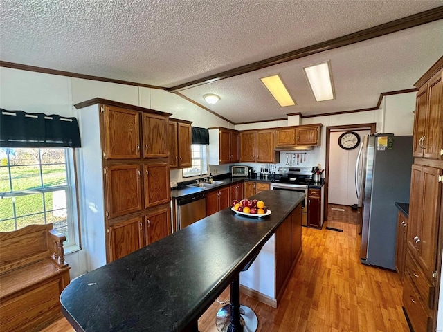 kitchen with lofted ceiling with beams, crown molding, a textured ceiling, appliances with stainless steel finishes, and light hardwood / wood-style floors