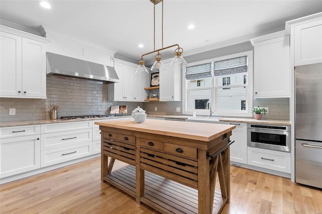 kitchen featuring white cabinets, ornamental molding, range hood, decorative light fixtures, and stainless steel appliances