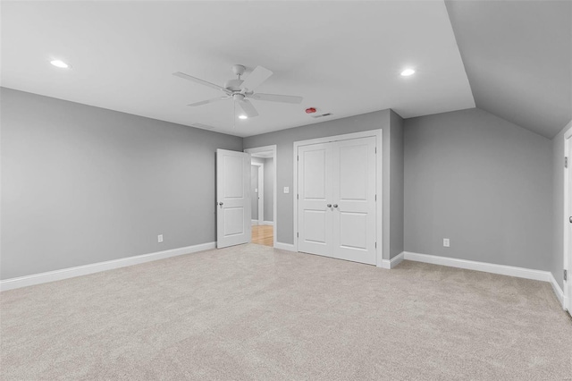 unfurnished bedroom featuring light carpet, a closet, vaulted ceiling, and ceiling fan