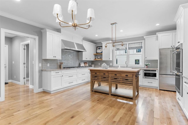 kitchen featuring white cabinetry, hanging light fixtures, wall chimney range hood, light hardwood / wood-style flooring, and crown molding