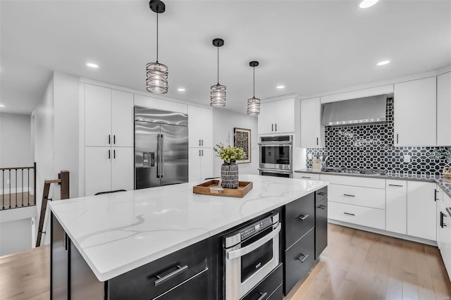 kitchen with stainless steel appliances, decorative light fixtures, white cabinets, a center island, and light hardwood / wood-style floors