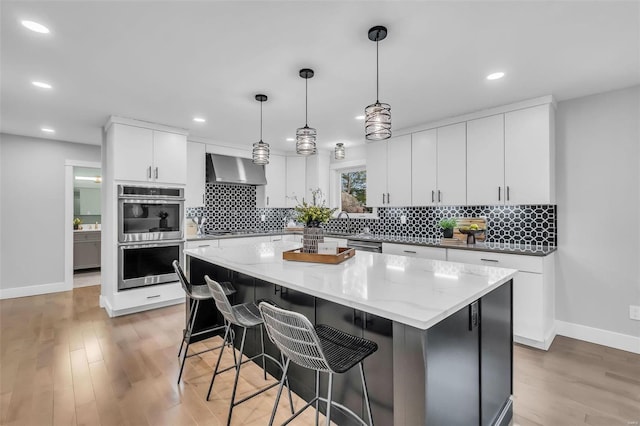 kitchen featuring white cabinetry, hanging light fixtures, wall chimney range hood, a kitchen island, and light wood-type flooring