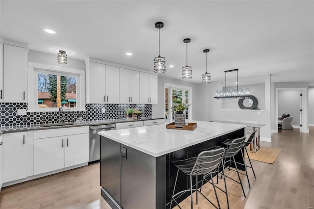 kitchen featuring white cabinetry, dishwasher, sink, a kitchen island, and light wood-type flooring