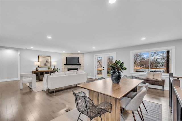 dining area featuring a stone fireplace, light wood-type flooring, and french doors