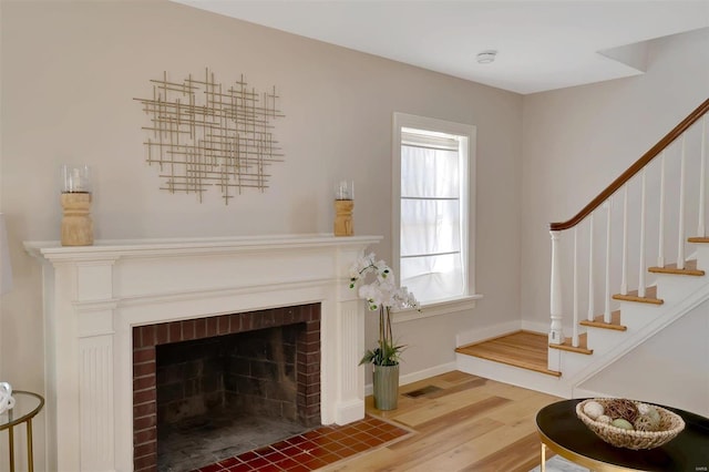 unfurnished living room featuring hardwood / wood-style flooring and a brick fireplace