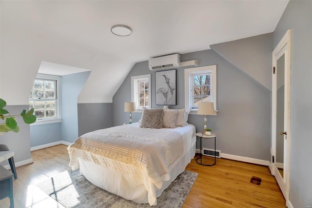 bedroom with a wall mounted AC, light wood-type flooring, vaulted ceiling, and multiple windows