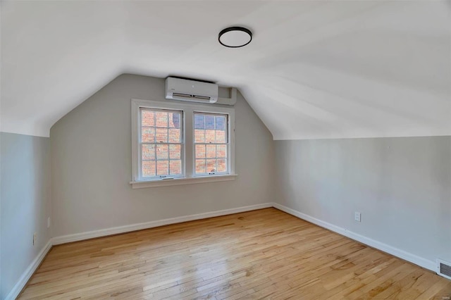 additional living space featuring light hardwood / wood-style floors, lofted ceiling, and a wall unit AC