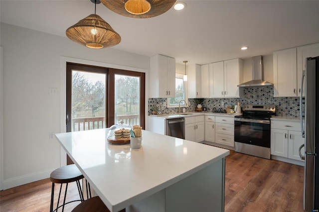 kitchen featuring white cabinetry, appliances with stainless steel finishes, pendant lighting, and wall chimney exhaust hood