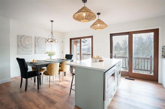 kitchen with pendant lighting, a kitchen breakfast bar, a center island, stainless steel microwave, and light wood-type flooring