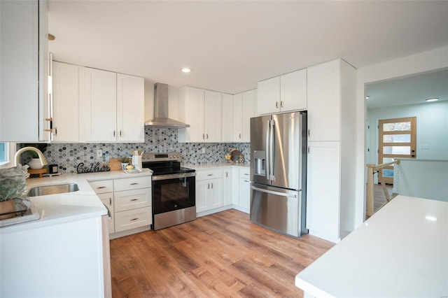 kitchen with stainless steel appliances, white cabinetry, and wall chimney range hood