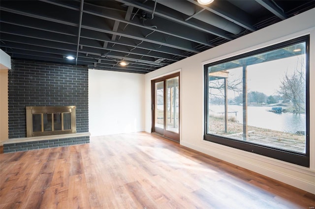 unfurnished living room with a brick fireplace, wood-type flooring, and a water view