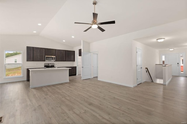 kitchen with appliances with stainless steel finishes, dark brown cabinets, vaulted ceiling, a center island with sink, and light hardwood / wood-style floors