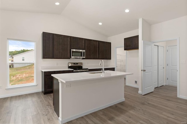 kitchen with stainless steel appliances, vaulted ceiling, a kitchen island with sink, sink, and light hardwood / wood-style floors