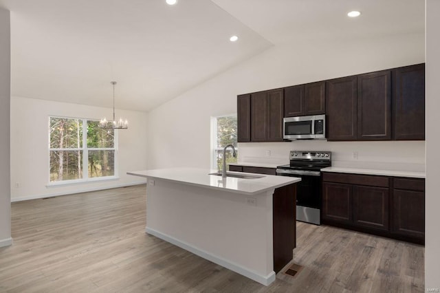 kitchen with appliances with stainless steel finishes, sink, light hardwood / wood-style floors, hanging light fixtures, and an island with sink