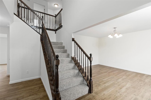 stairway featuring a towering ceiling, hardwood / wood-style flooring, and an inviting chandelier