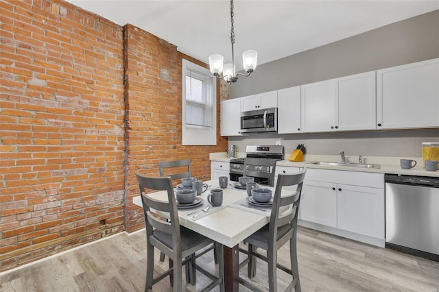 kitchen featuring sink, stainless steel appliances, brick wall, decorative light fixtures, and white cabinets