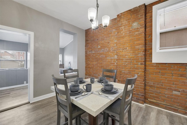 dining area featuring dark hardwood / wood-style flooring, a notable chandelier, and brick wall