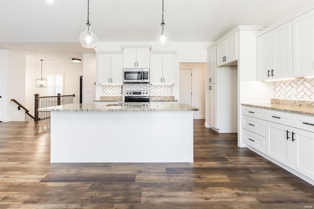 kitchen featuring light stone countertops, appliances with stainless steel finishes, white cabinets, dark hardwood / wood-style floors, and hanging light fixtures