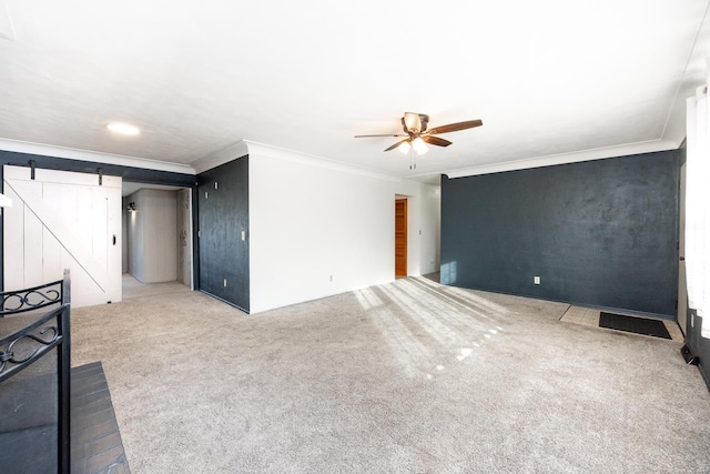 unfurnished living room with a barn door, light carpet, ceiling fan, and ornamental molding