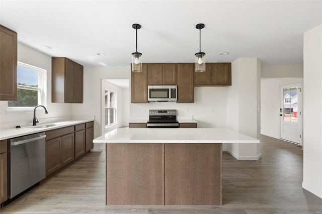 kitchen with dark hardwood / wood-style flooring, stainless steel appliances, sink, decorative light fixtures, and a kitchen island