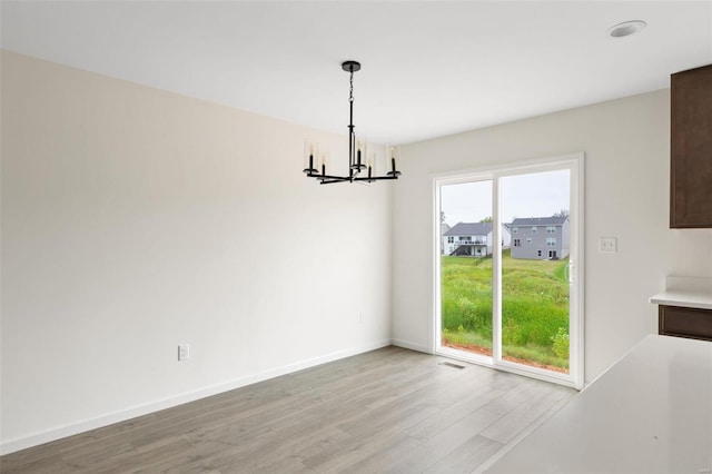 unfurnished dining area with a notable chandelier and light wood-type flooring