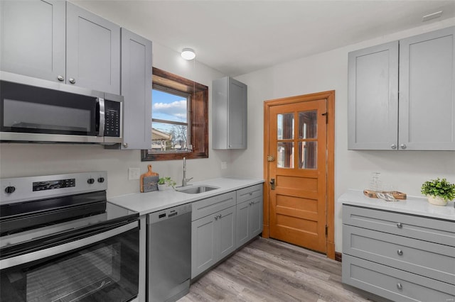 kitchen with light wood-type flooring, stainless steel appliances, gray cabinetry, and sink