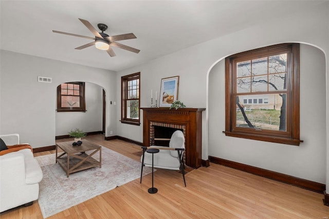 living room with ceiling fan, light hardwood / wood-style floors, and a brick fireplace