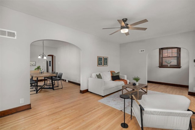 living room with ceiling fan with notable chandelier and light wood-type flooring