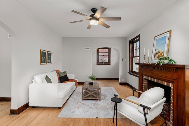 living room featuring a brick fireplace, ceiling fan, and light hardwood / wood-style flooring