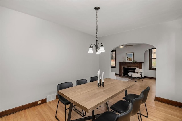 dining room featuring light hardwood / wood-style floors, ceiling fan with notable chandelier, and a brick fireplace