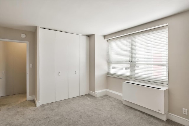 unfurnished bedroom with light colored carpet, radiator heating unit, and a closet