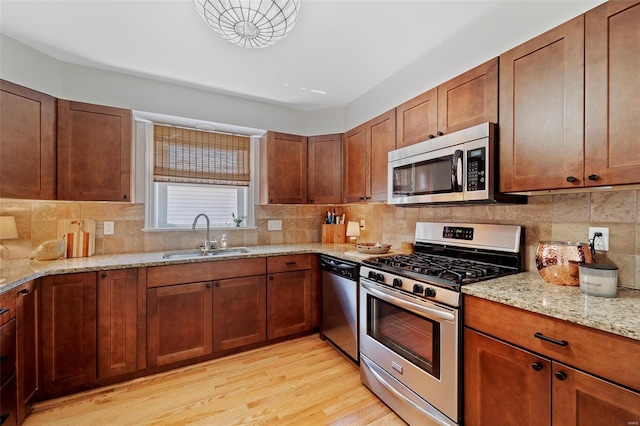 kitchen with sink, tasteful backsplash, light hardwood / wood-style floors, light stone counters, and stainless steel appliances