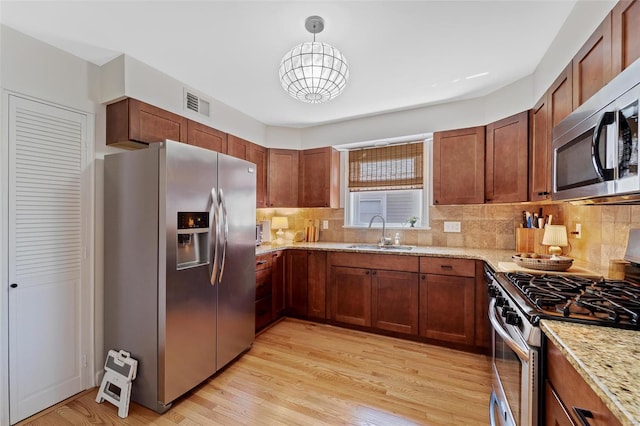 kitchen with appliances with stainless steel finishes, light wood-type flooring, light stone counters, sink, and hanging light fixtures