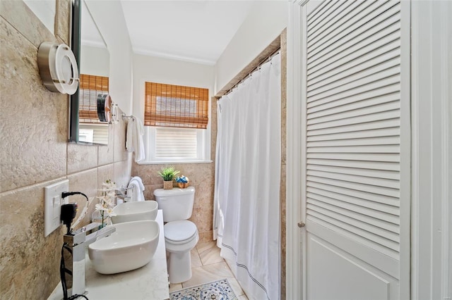 bathroom featuring tile patterned floors, double sink, a shower with curtain, tile walls, and toilet