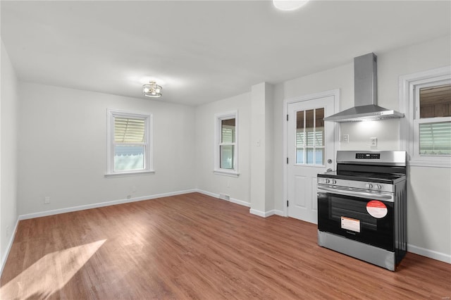 kitchen with wall chimney range hood, a healthy amount of sunlight, light hardwood / wood-style floors, and stainless steel range oven