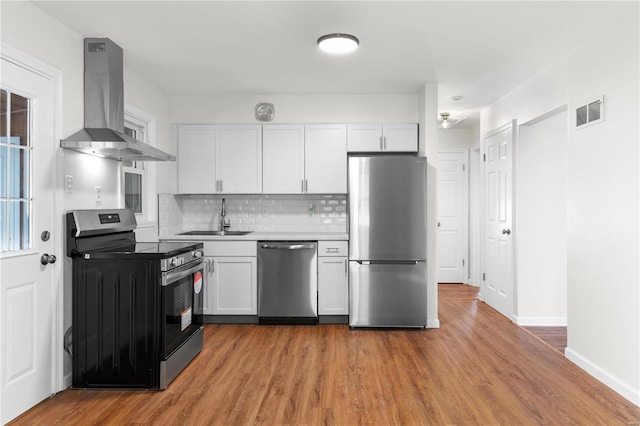 kitchen with light wood-type flooring, stainless steel appliances, sink, wall chimney range hood, and white cabinets