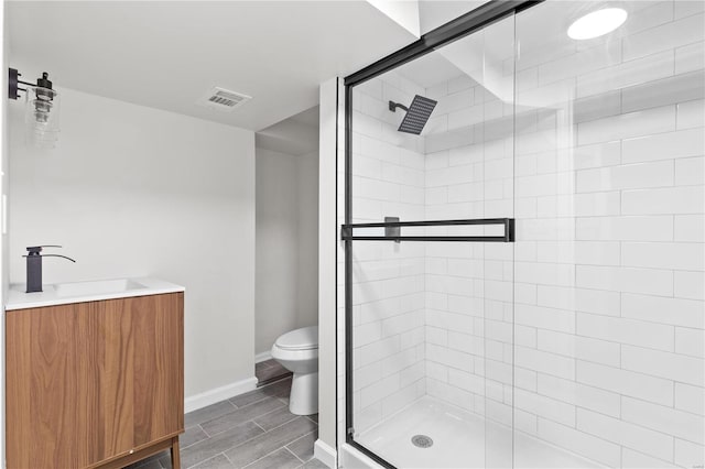 bathroom featuring a shower with door, vanity, and toilet